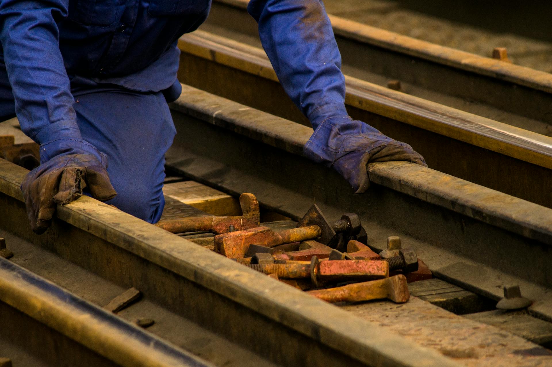 Close-up of worker in protective gear maintaining railway tracks with tools.