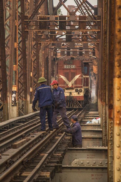 Free Industrial scene of workers maintaining railway tracks on a steel bridge with a locomotive in view. Stock Photo