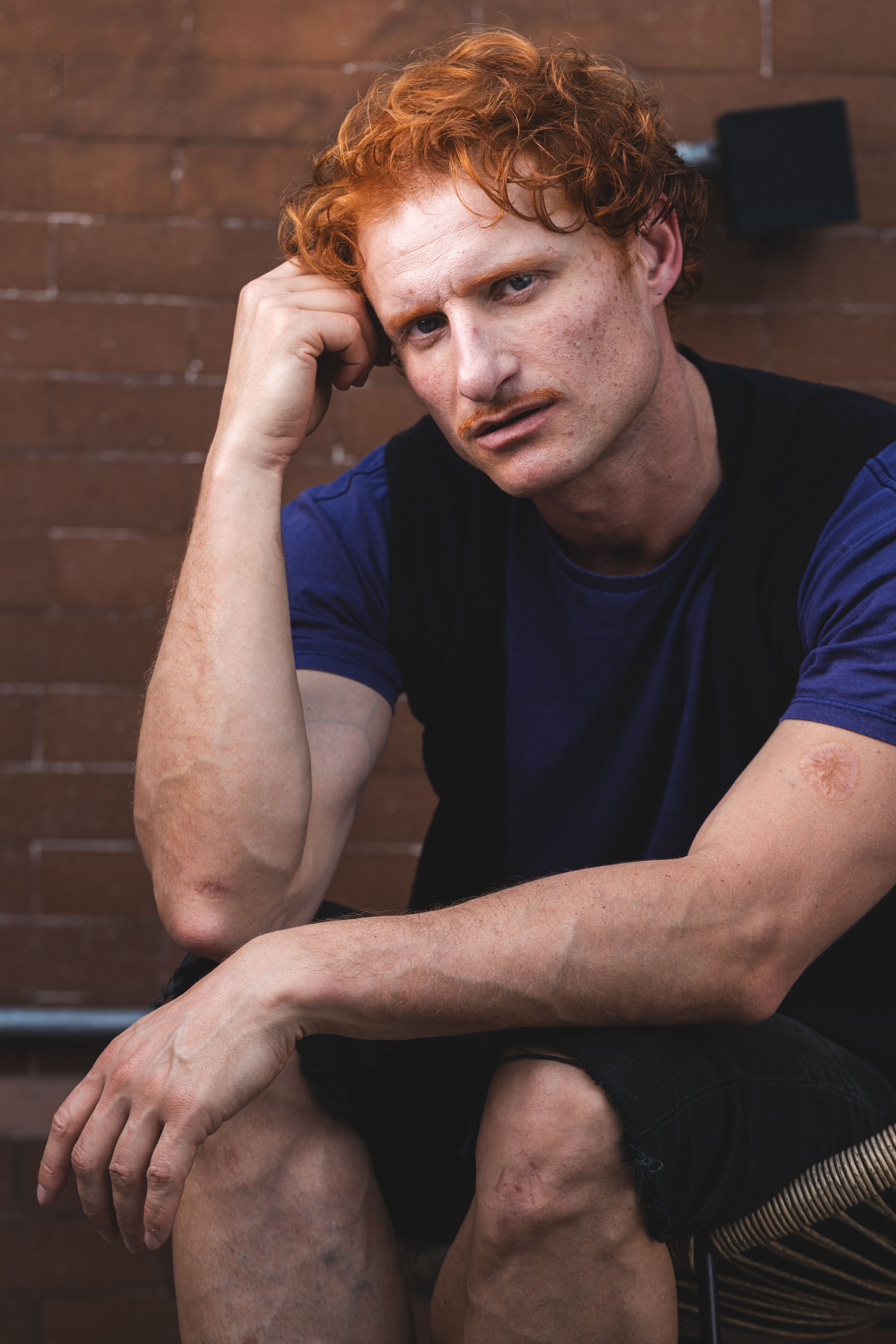 Young man sitting thoughtfully against a brick wall outdoors.