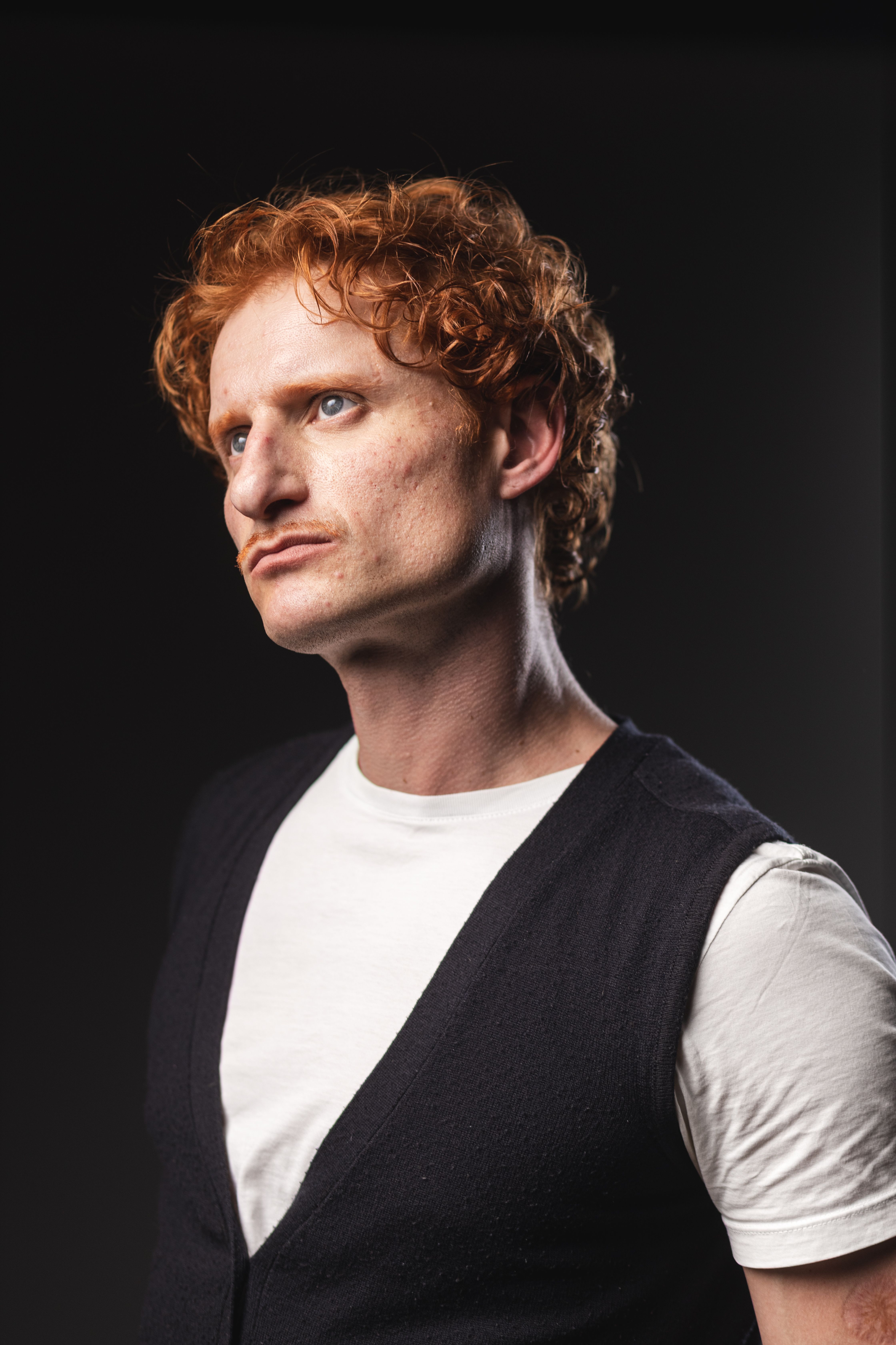 Dynamic portrait of a redheaded man in a thoughtful pose with dramatic lighting.