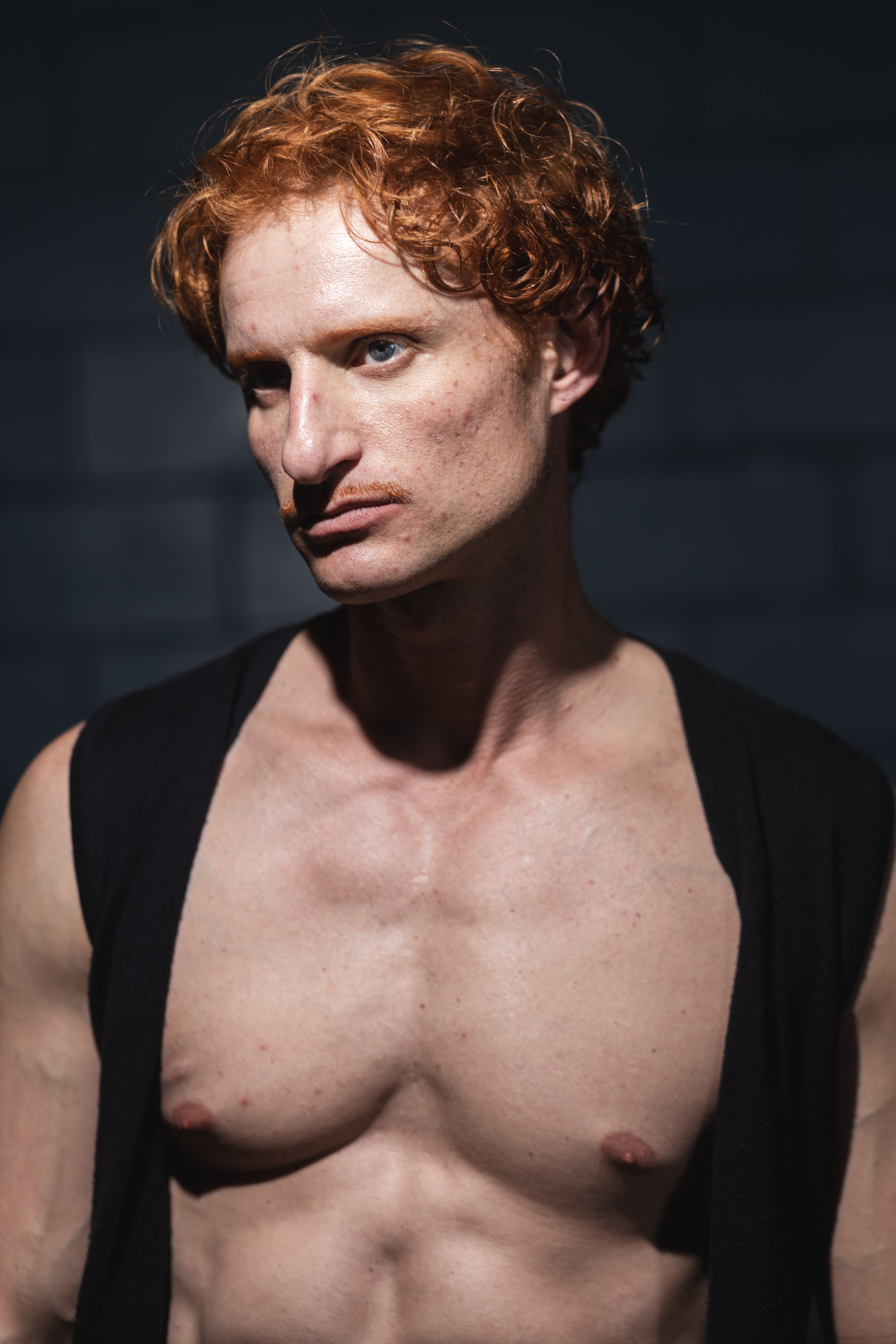 Cinematic portrait of a redheaded man in deep thought against dark background.