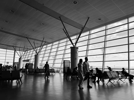 Black and white view of a busy airport terminal with travelers waiting and walking.