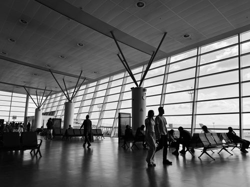 Free Black and white view of a busy airport terminal with travelers waiting and walking. Stock Photo