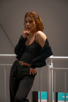 A fashionable young woman poses confidently indoors with dramatic lighting.