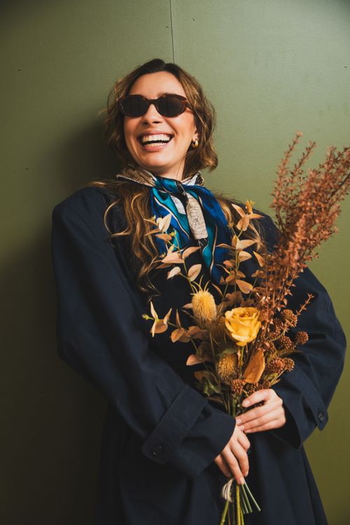 Free A fashionable woman in sunglasses holds a bouquet, exuding joy. Perfect for lifestyle and fashion themes. Stock Photo