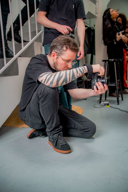 Free Man photographing indoors with camera, surrounded by people, showcasing focus and creativity. Stock Photo