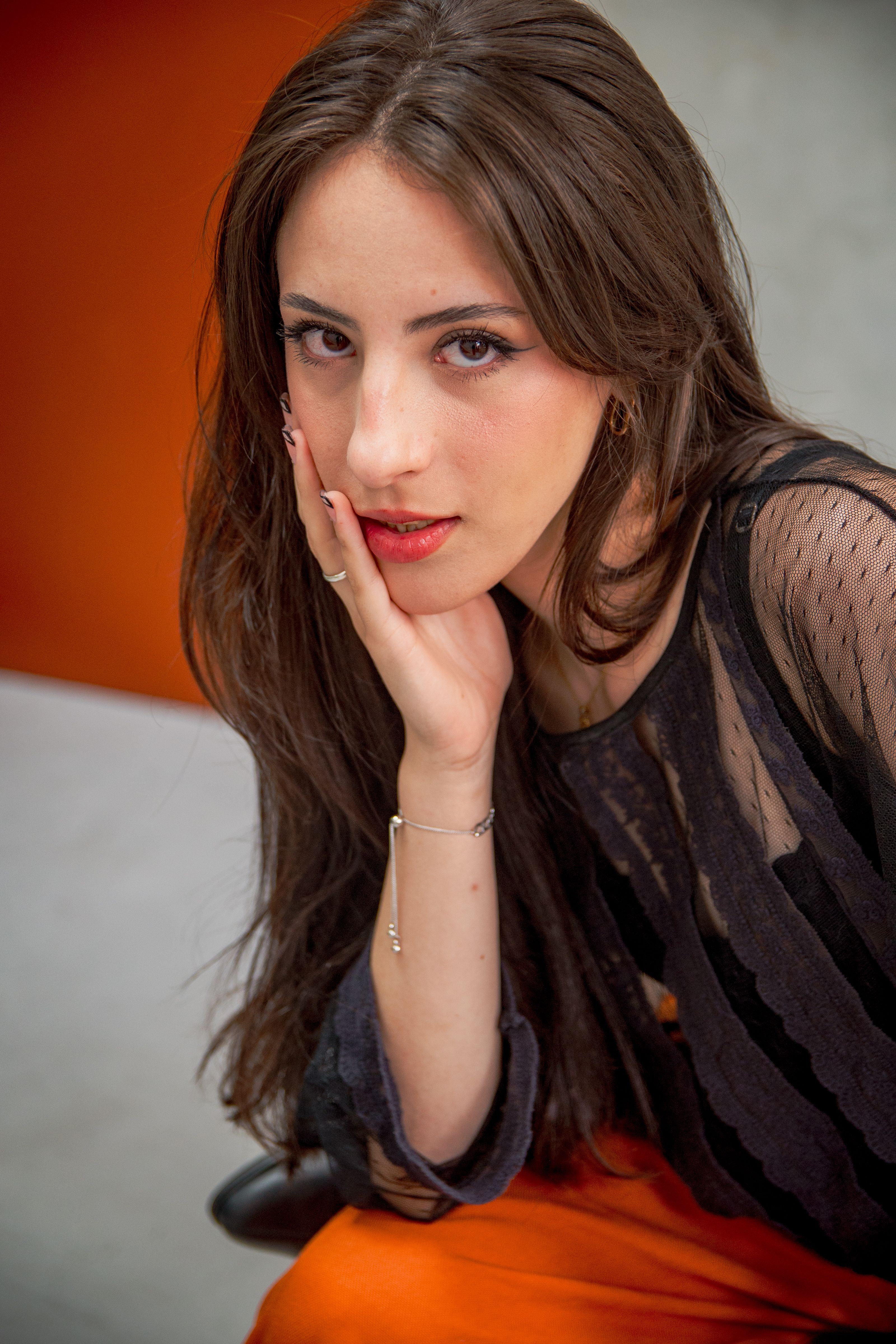 Close-up portrait of a young woman with long hair and stylish outfit, modeling indoors.