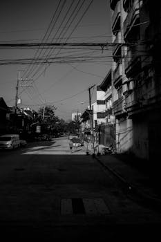 Dramatic black and white shot of a quiet city street with shadows and power lines.
