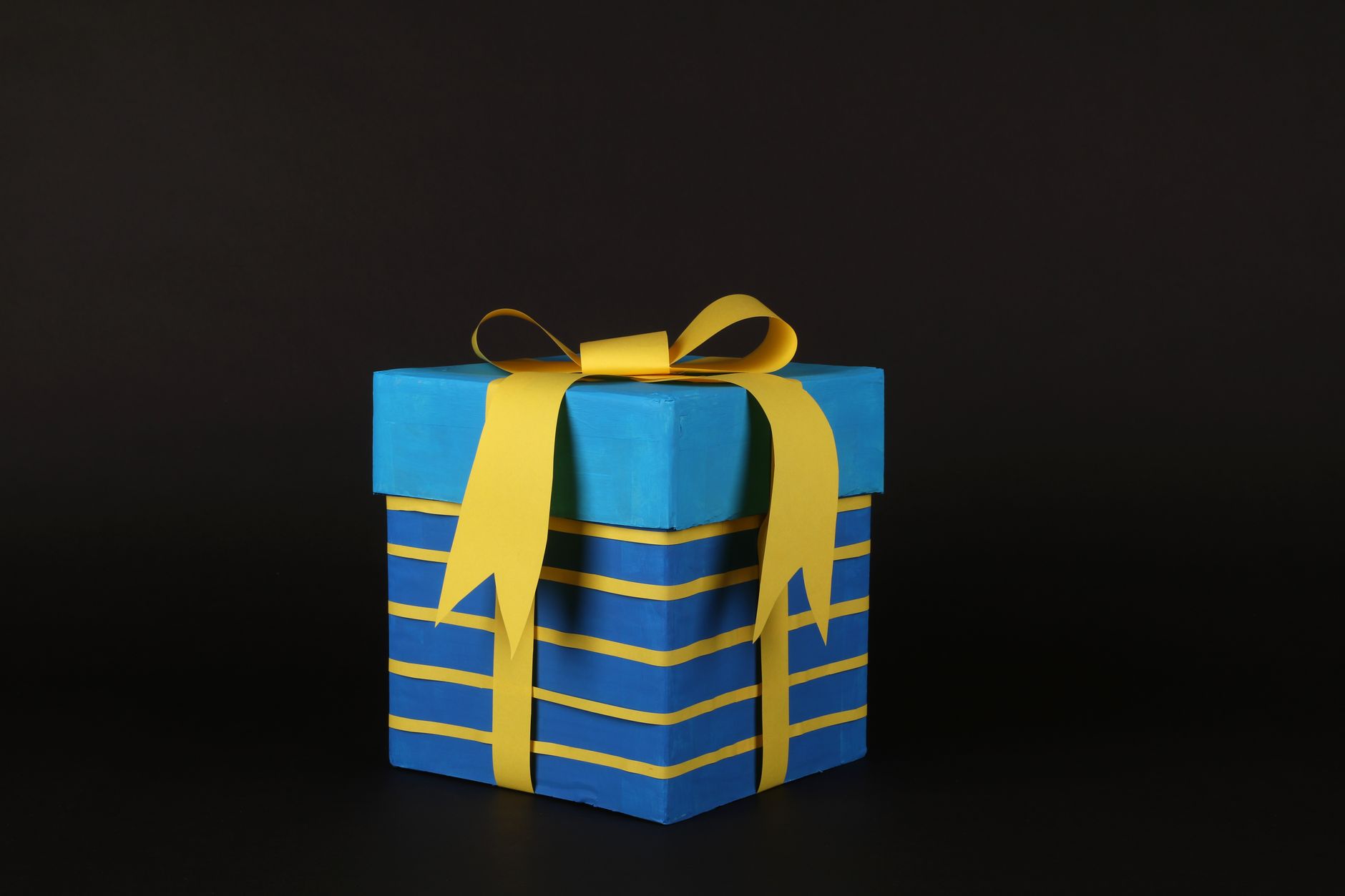 Vibrant blue gift box wrapped in yellow ribbon on black background for celebrations.