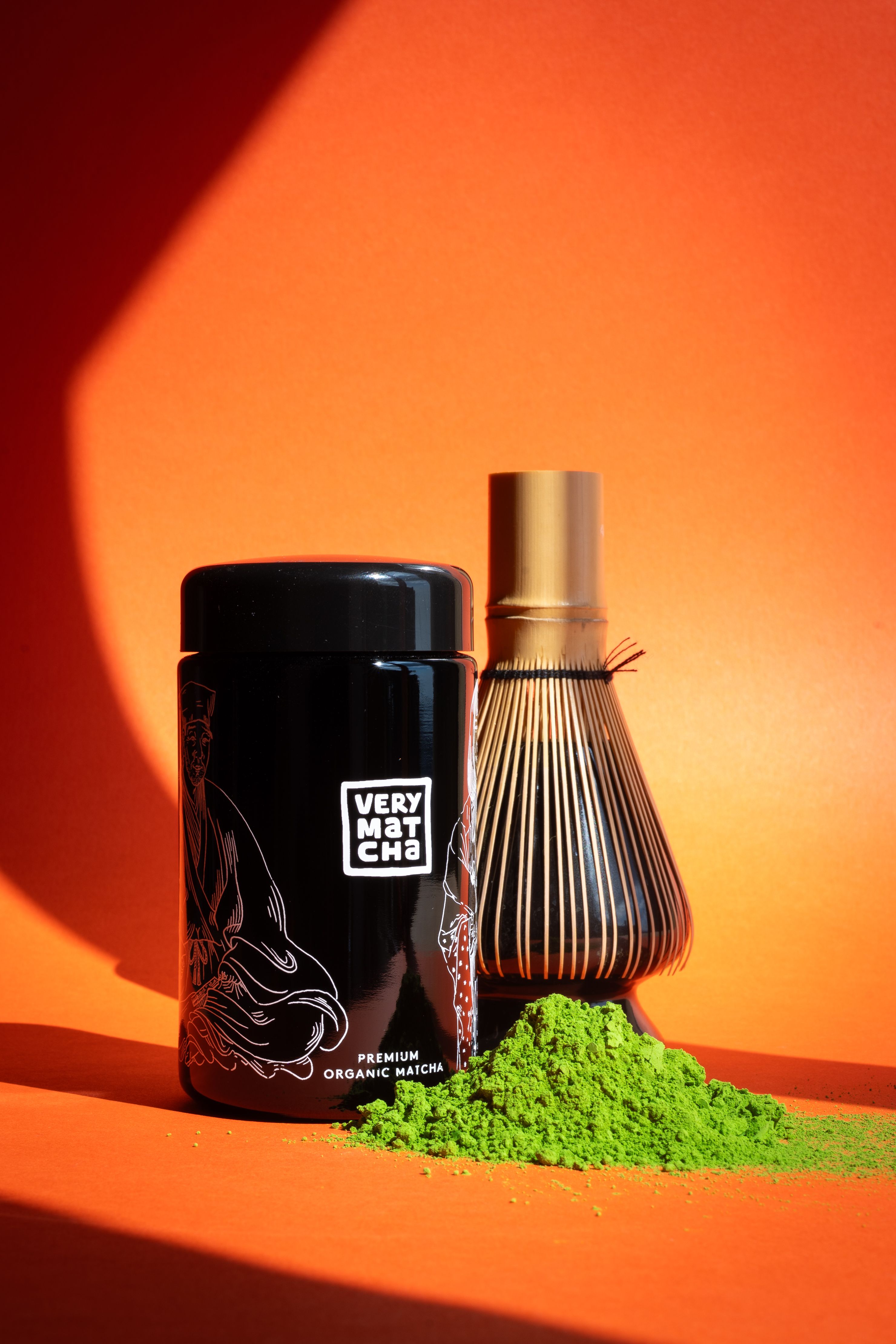 Organic matcha powder with chasen whisk against a bold orange backdrop, highlighting Japanese tea culture.