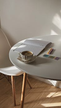 Minimalist workspace featuring a cup of coffee on a table with an open notebook and colored pencils.