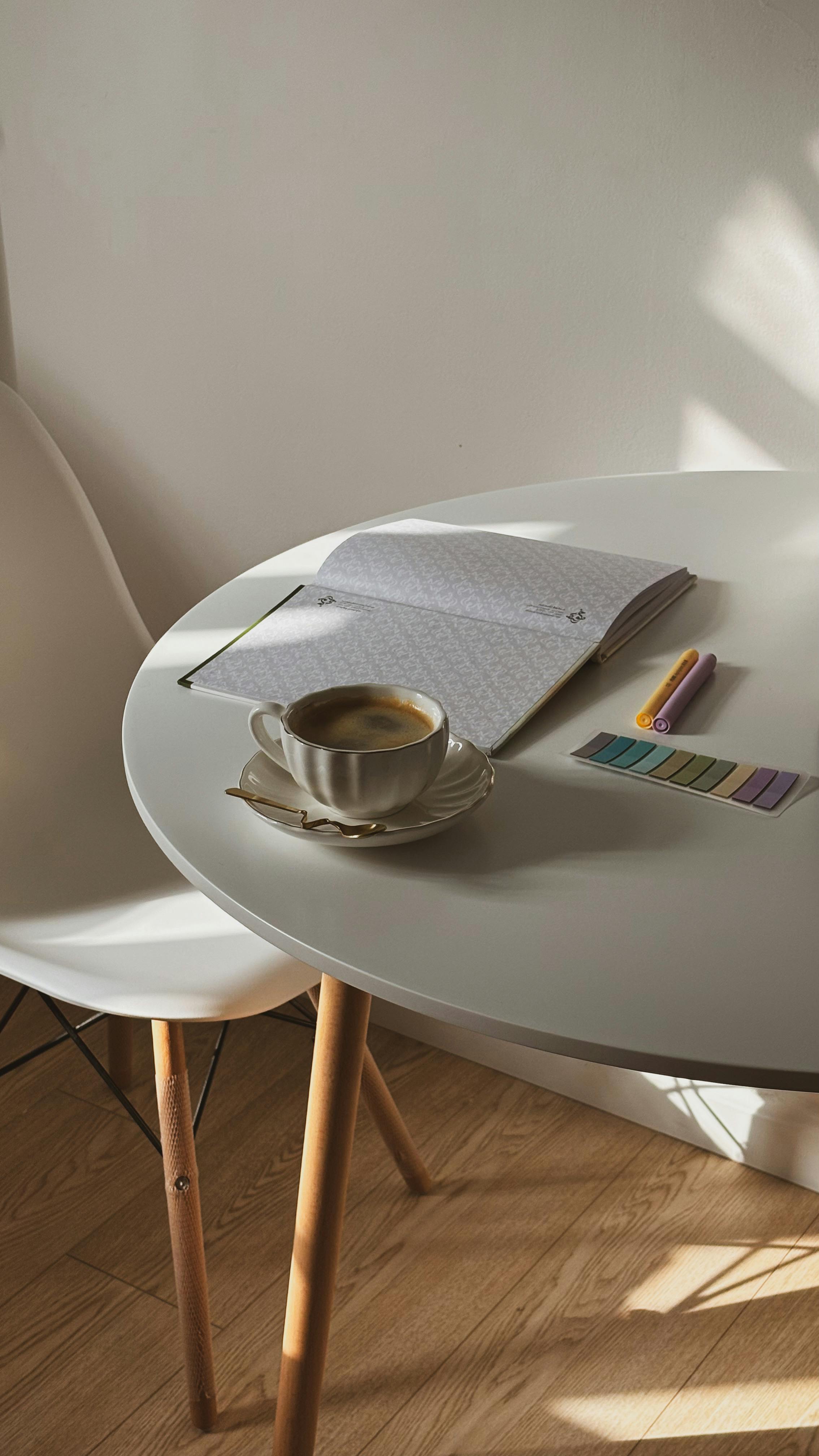 Kostnadsfria Minimalistisk arbetsyta med en kopp kaffe på ett bord med en öppen anteckningsbok och färgpennor. Stock foto