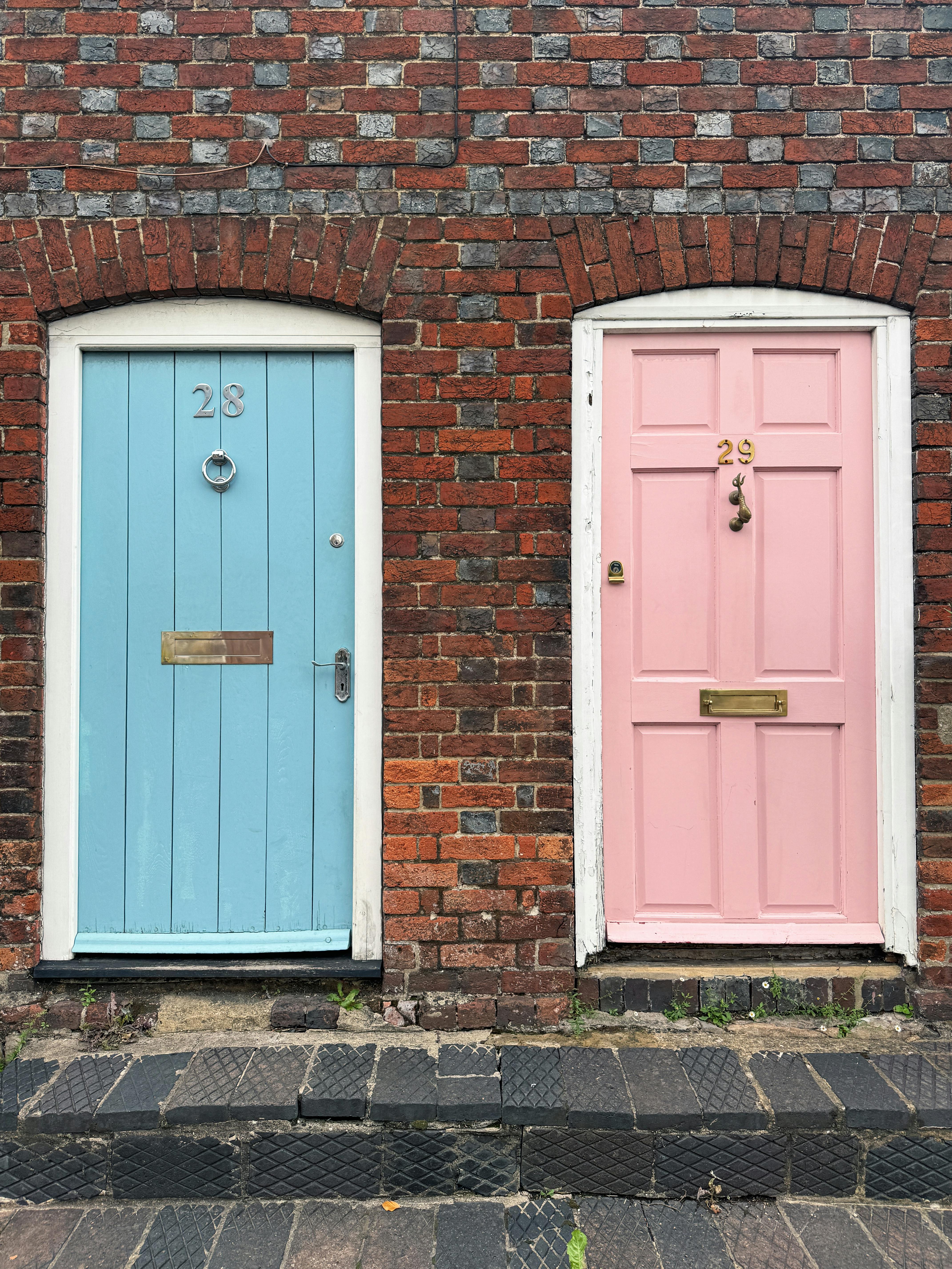 Charming pastel blue and pink doors on a rustic brick wall in Marlborough, UK.