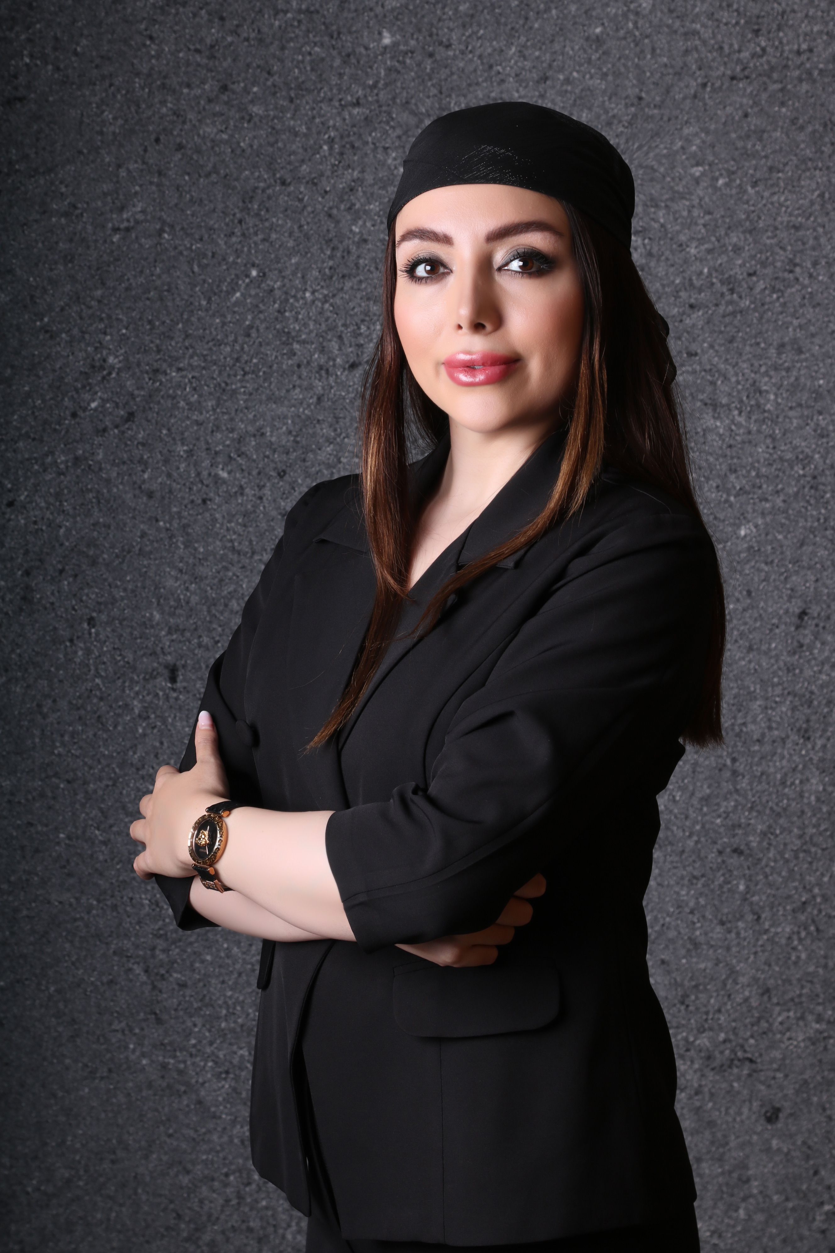Portrait of a confident woman in black with arms crossed against a textured background.