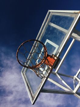 Low-angle view of an old basketball hoop with rust against a clear blue sky, capturing outdoor sports vibe.
