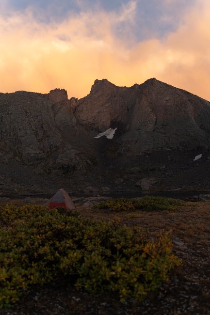 Ultralight two person tent pitched on alpine tundra near a rocky ridgeline at sunrise
