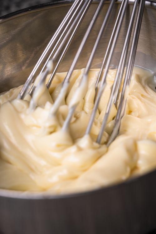 Free A stainless steel whisk blending rich creamy sauce in a metal bowl, signifying cooking action. Stock Photo