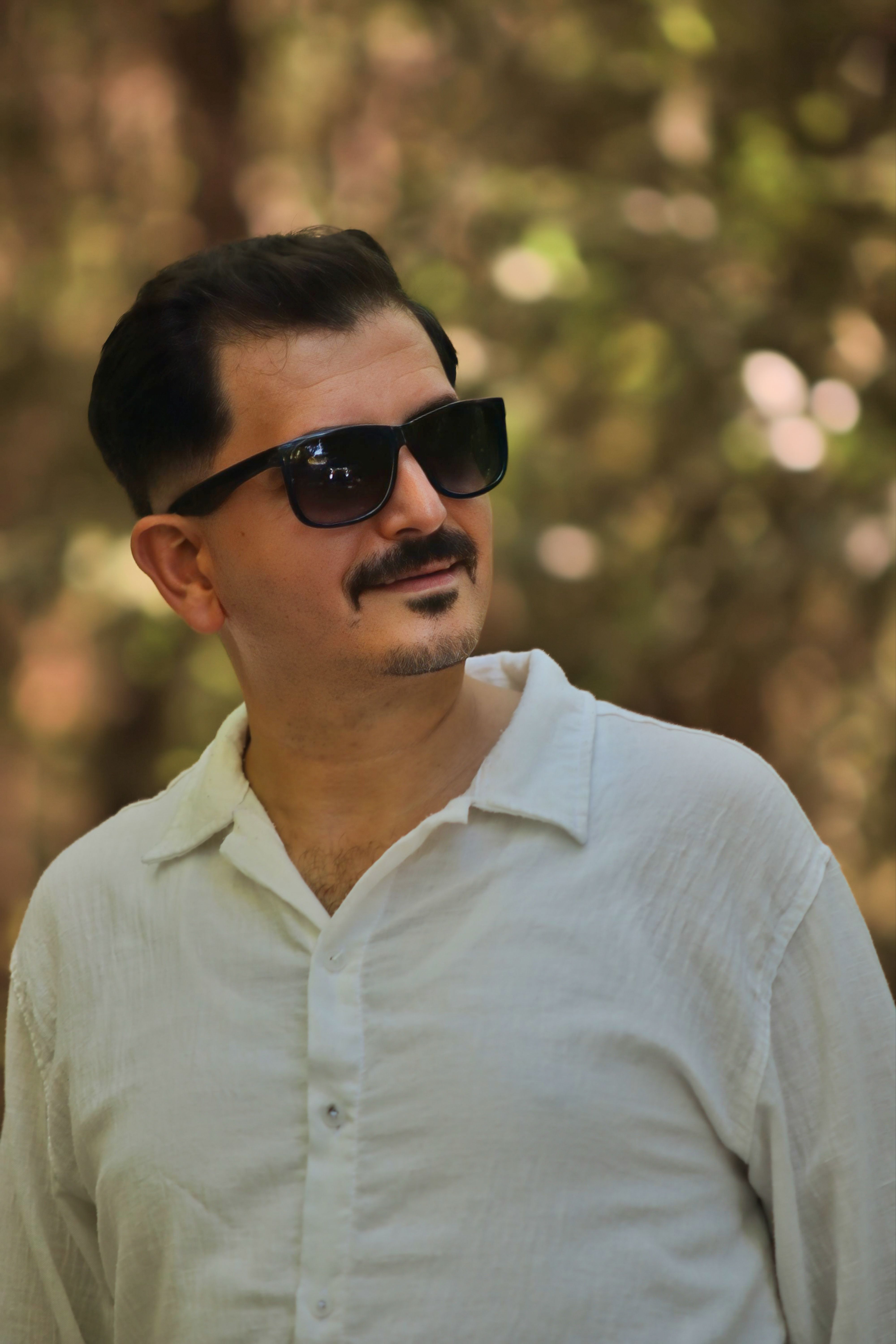 A man wearing sunglasses and a white shirt enjoying a sunny day outdoors.