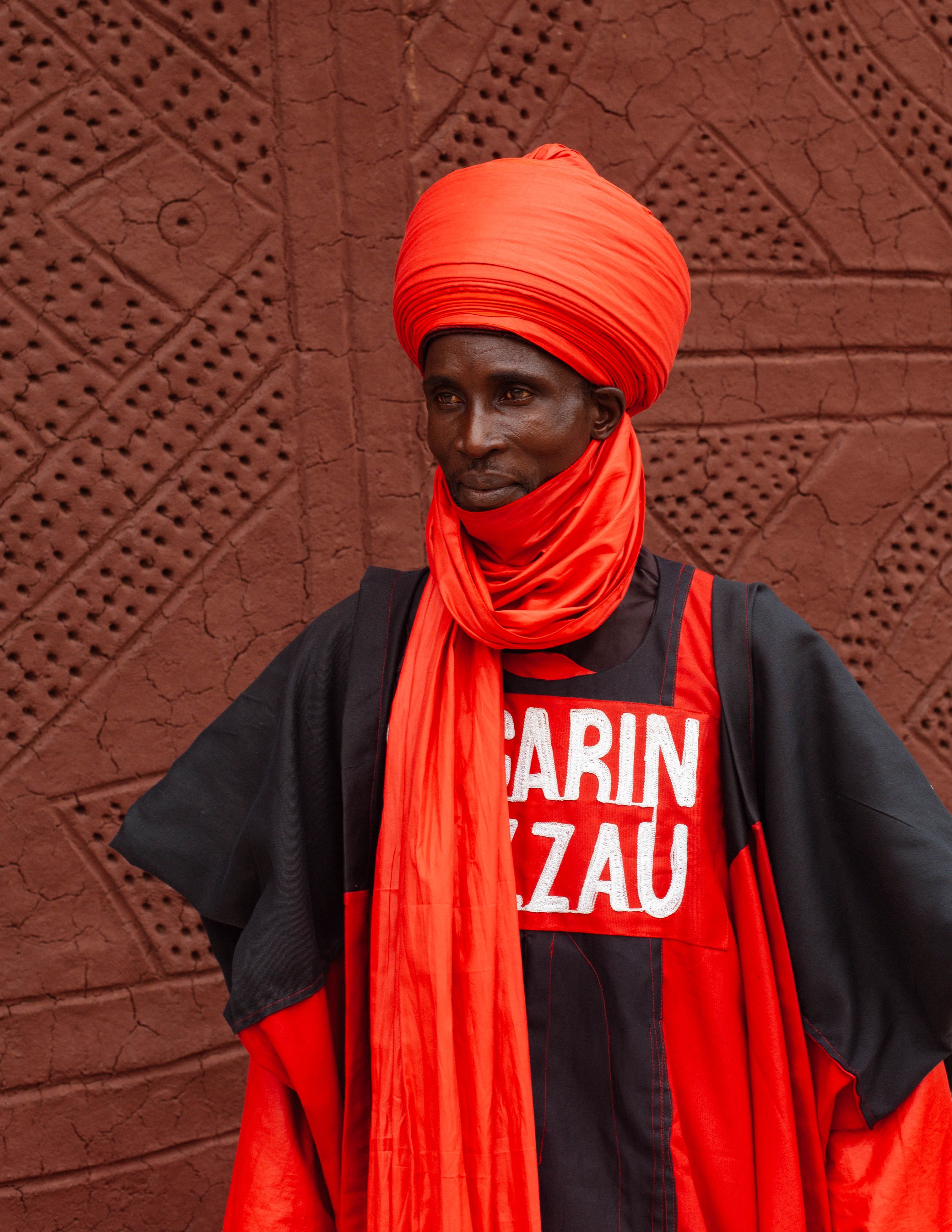 Portrait of a man in vibrant traditional attire against a textured wall.