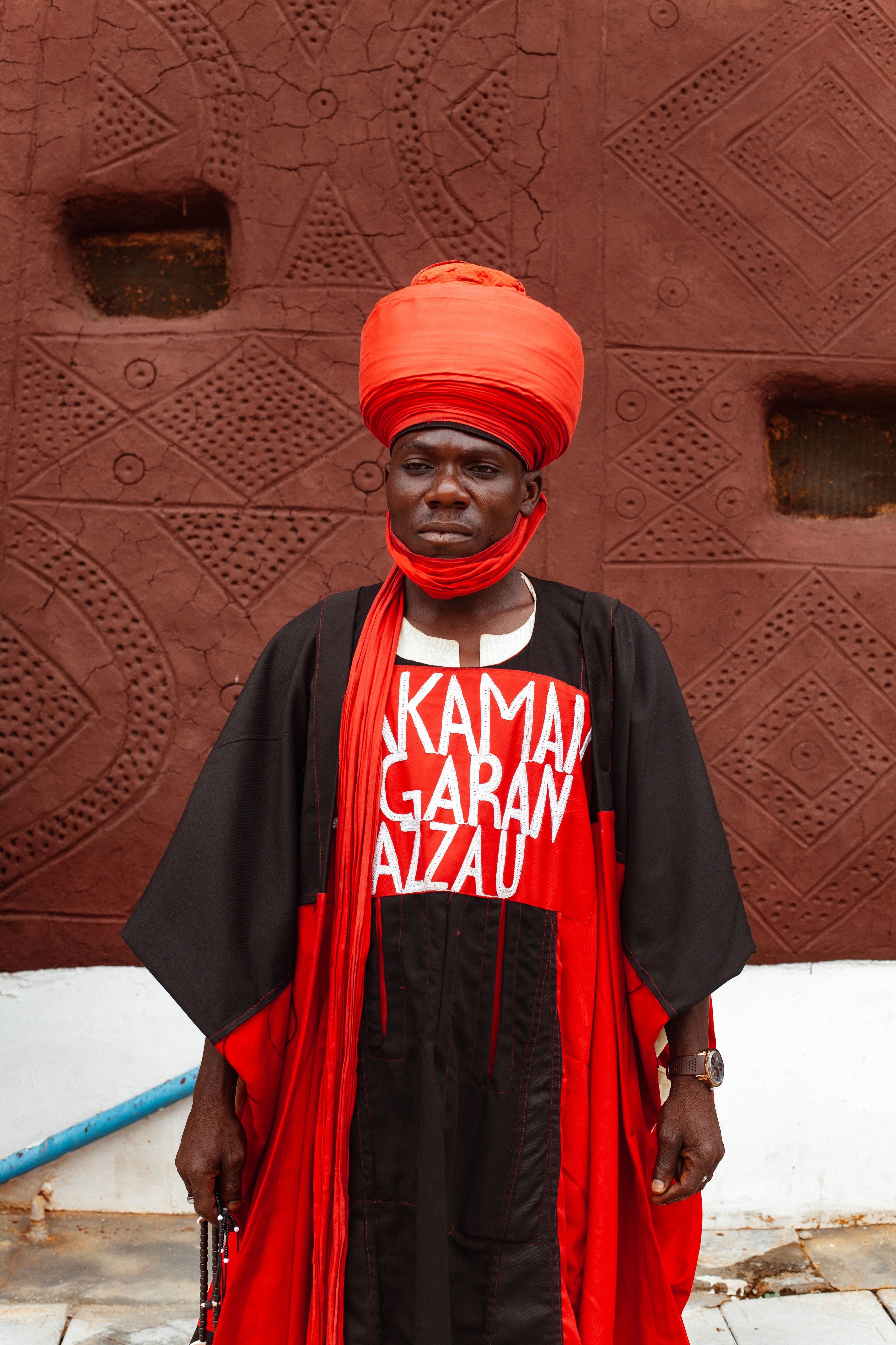 Portrait of an adult man in traditional African attire with a bold red turban and vibrant clothing.