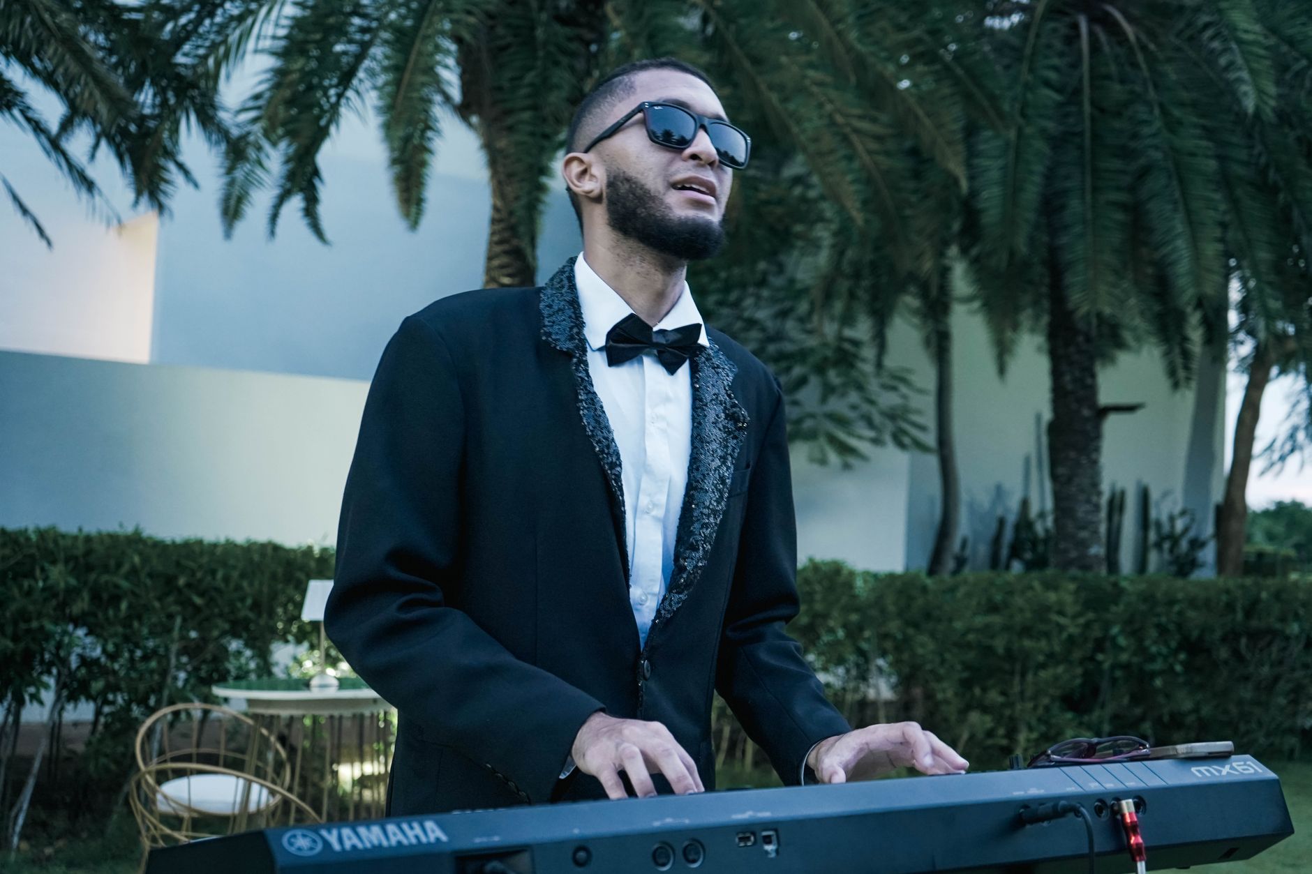 marassi summer event planner — Stylish musician in formal attire playing a keyboard outdoors under palm trees.