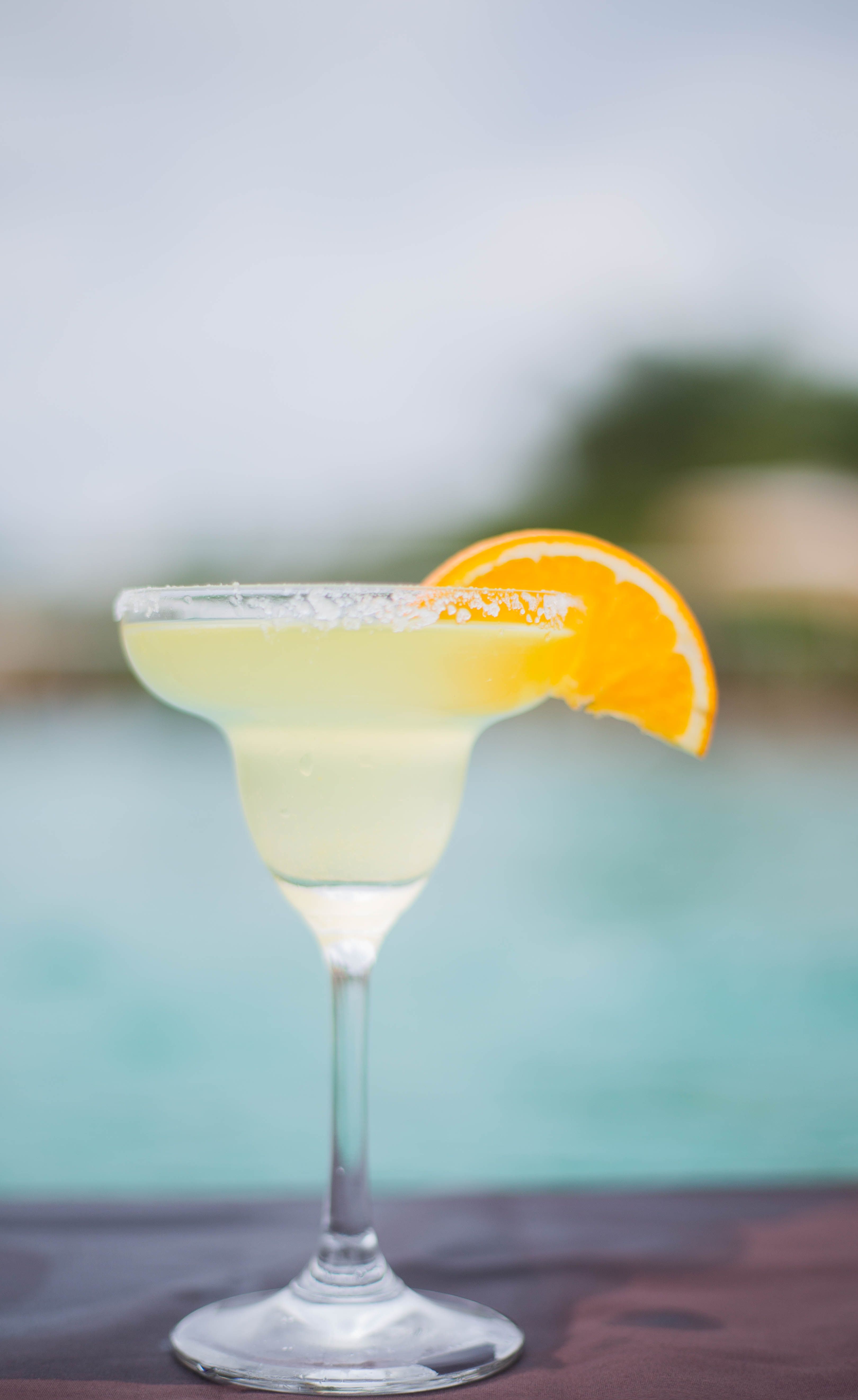 Close-up of a margarita cocktail with an orange slice by a pool, perfect for summer relaxation.
