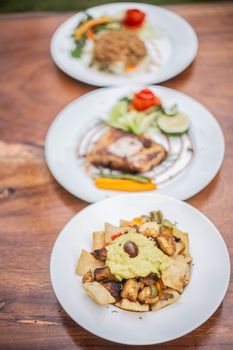 Three artfully plated gourmet dishes on a wooden table, showcasing diverse cuisines.