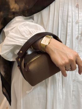A woman's hand wearing a gold watch holds a stylish brown purse, showcasing fashion elegance.