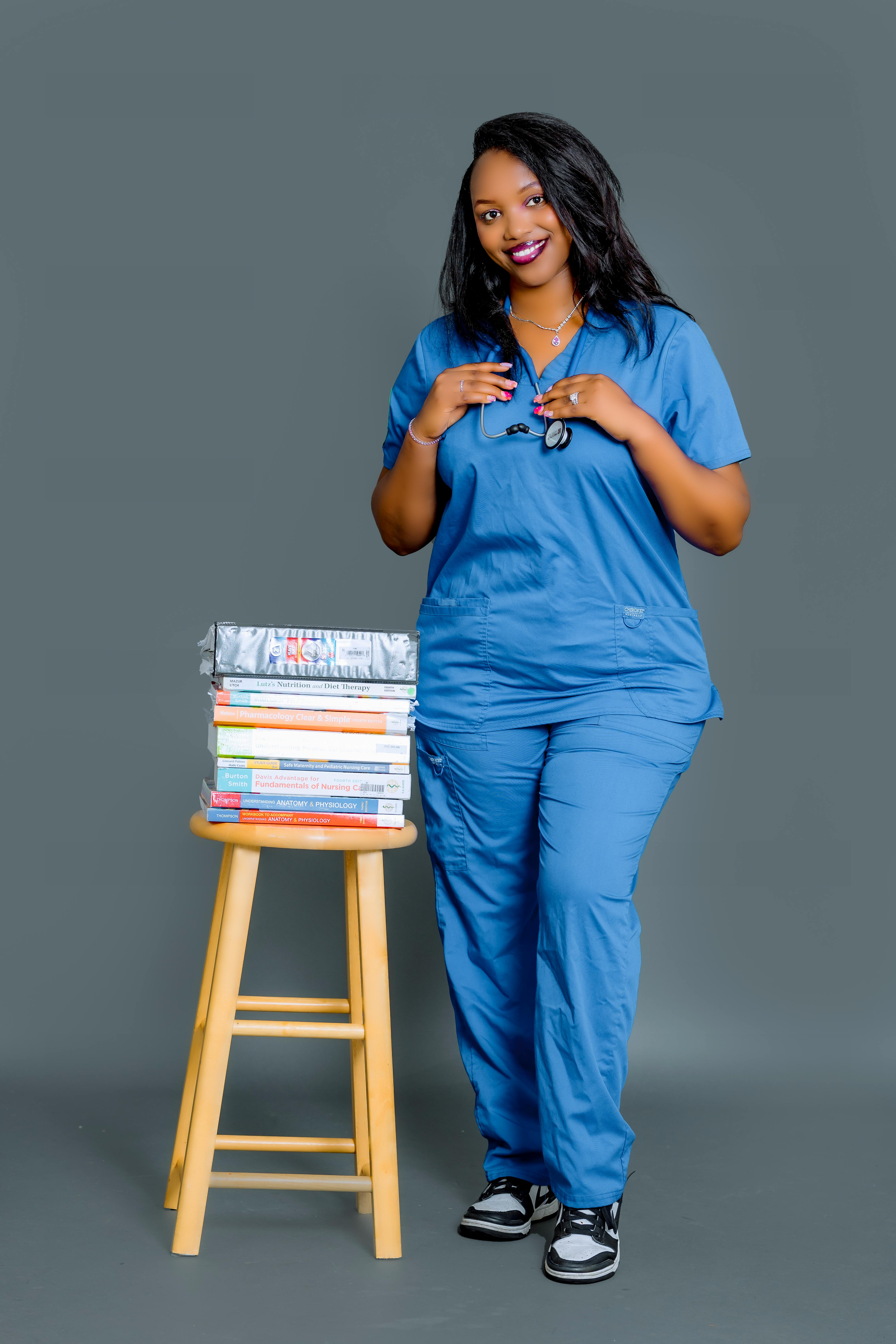 Happy female nurse in blue scrubs with stethoscope and textbooks on stool.