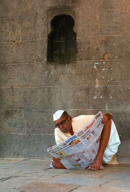 Free Elderly man reading a newspaper against ancient temple wall in Solapur, India. Stock Photo