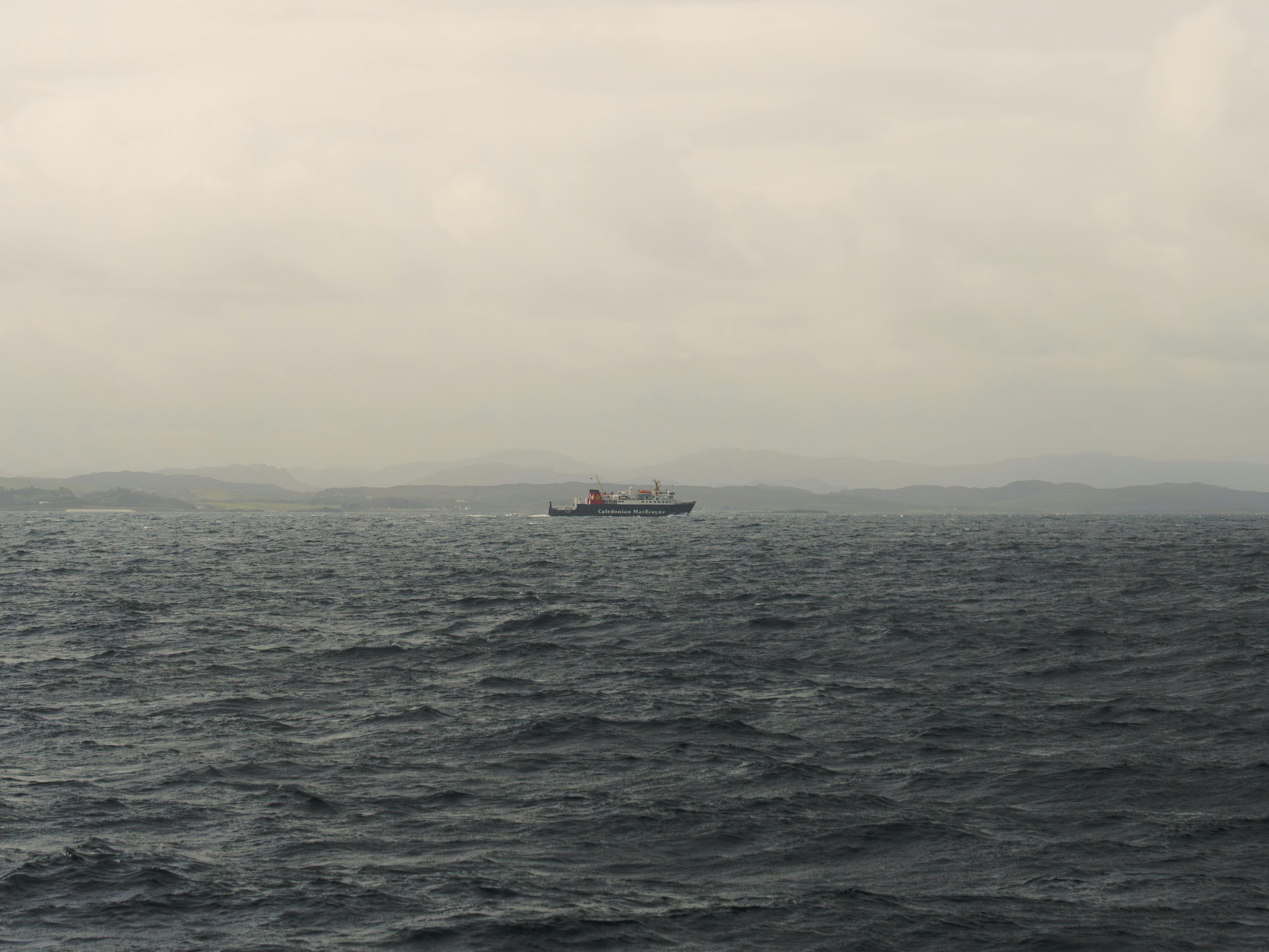 A ferry sailing on the dark sea with Scotland's mountainous coastline in the distance under a moody sky.