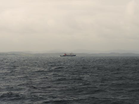 A ferry sailing on the dark sea with Scotland's mountainous coastline in the distance under a moody sky.