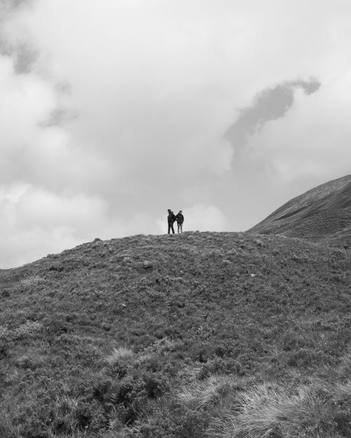 Free Two hikers standing atop a grassy hill in Scotland, captured in striking black and white. Stock Photo