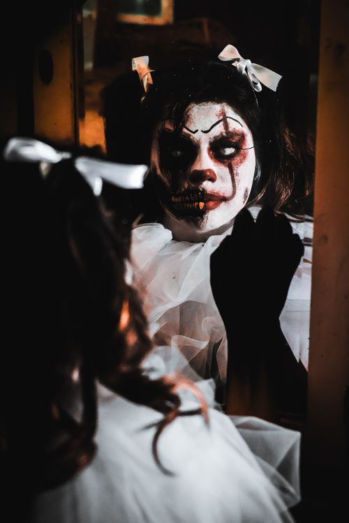 Free A person in scary clown makeup reflecting in a mirror, creating a haunting Halloween vibe. Stock Photo
