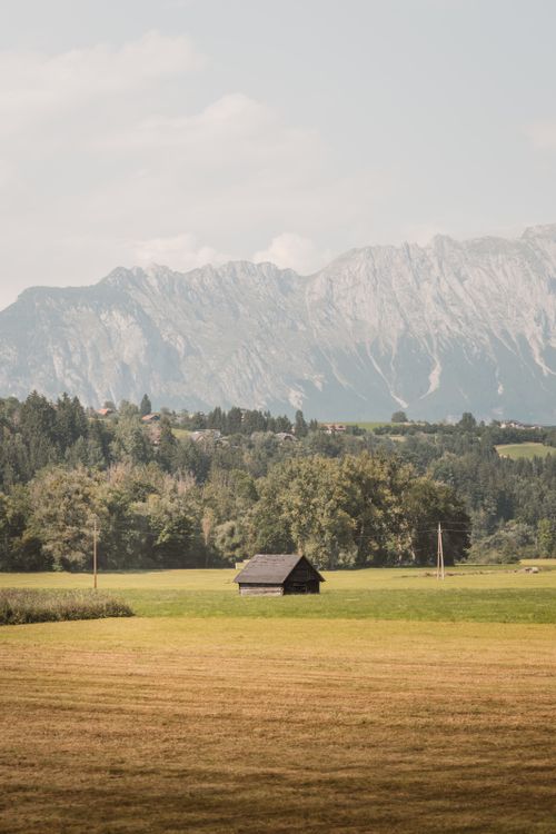 Free A solitary cabin in an open meadow with scenic mountain backdrop, offering a peaceful escape. Stock Photo