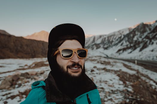 在户外雪山风景中，一位脸上有胡须、戴着太阳镜的男子微笑着