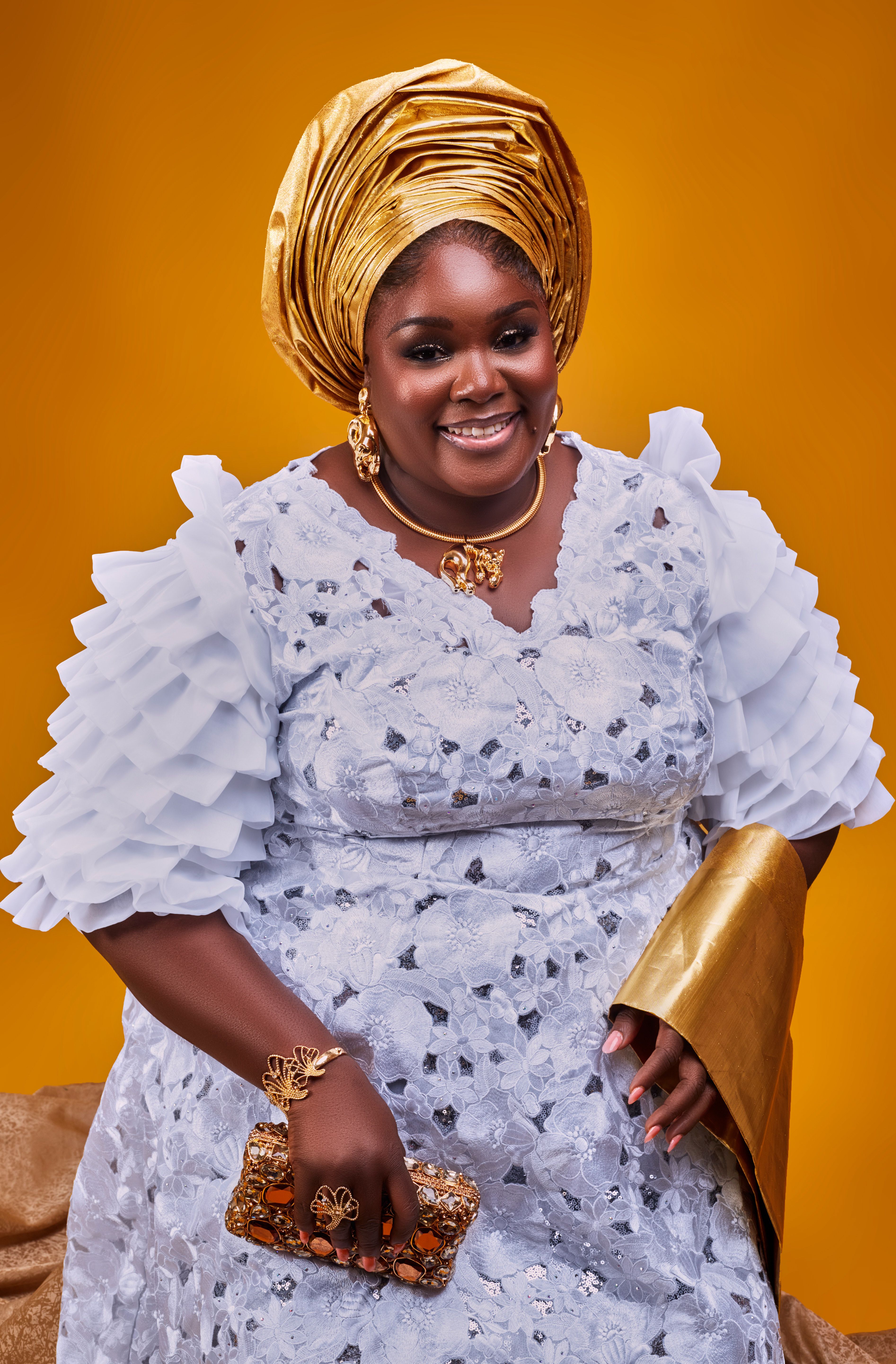 African woman in ornate traditional attire with golden accessories, joyful expression.