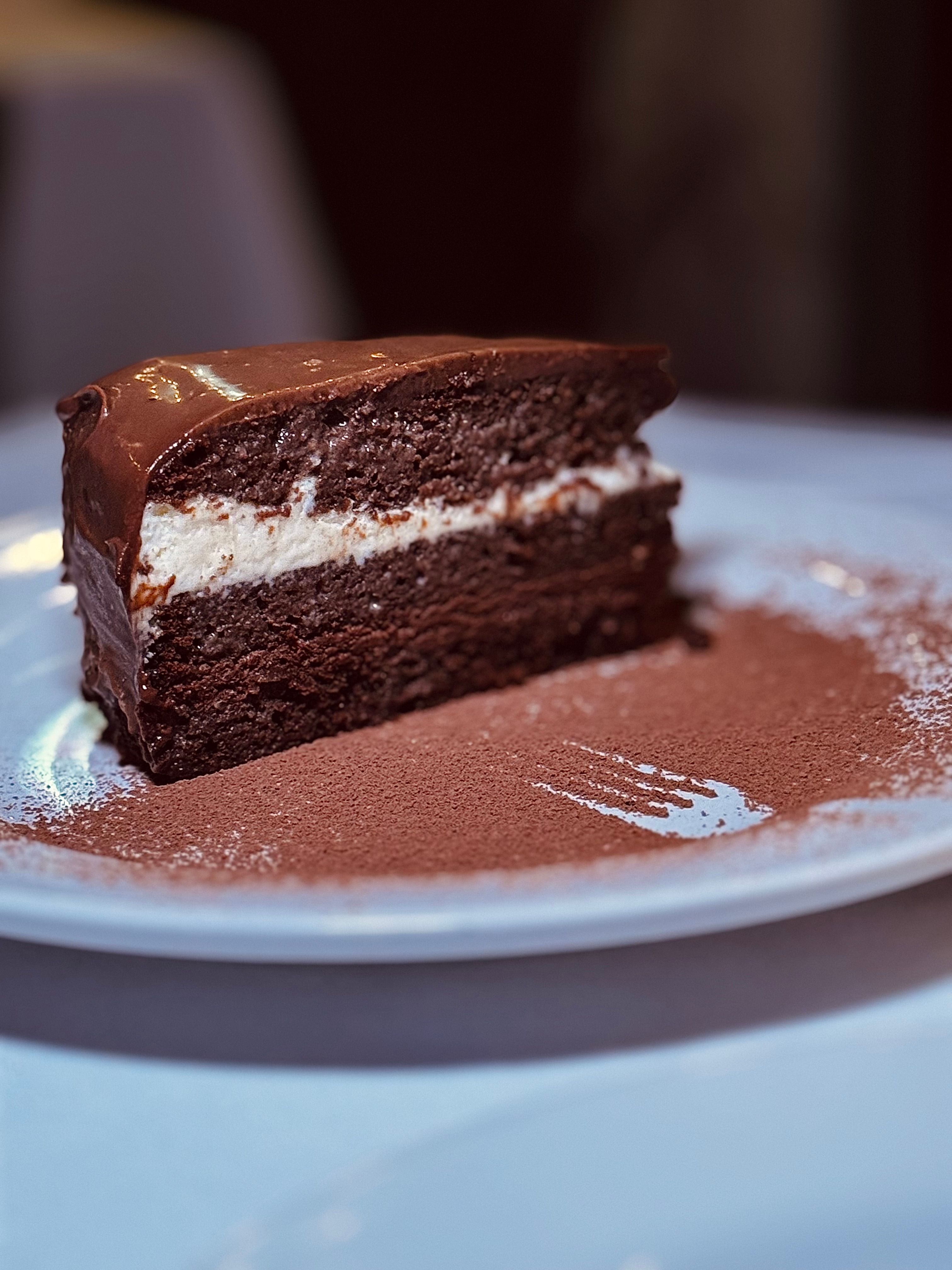 A rich chocolate cake slice with creamy filling on a white plate, perfect for dessert lovers.