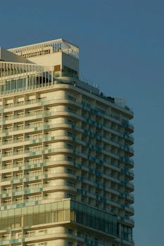A modern high-rise building with a glass facade and balconies captured at sunset under a clear blue sky.