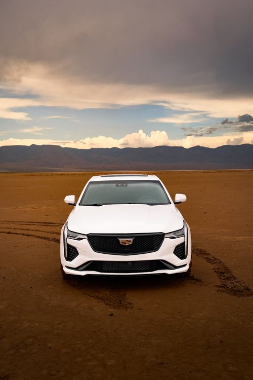 Free A sleek white car on a desolate desert landscape with dramatic clouds overhead. Stock Photo