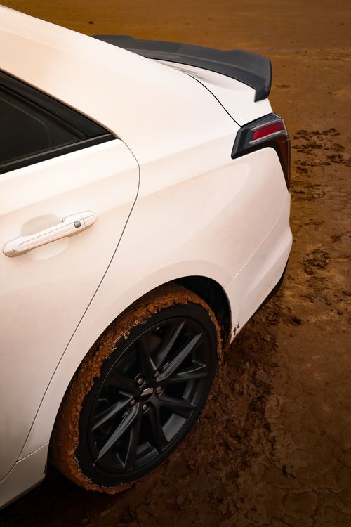 Free Close-up of a white car with muddy tires on a textured dirt road, showcasing rear design. Stock Photo