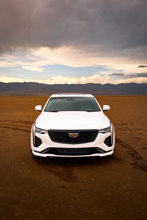 Free White luxury car parked on a vast desert landscape with dramatic skies. Stock Photo