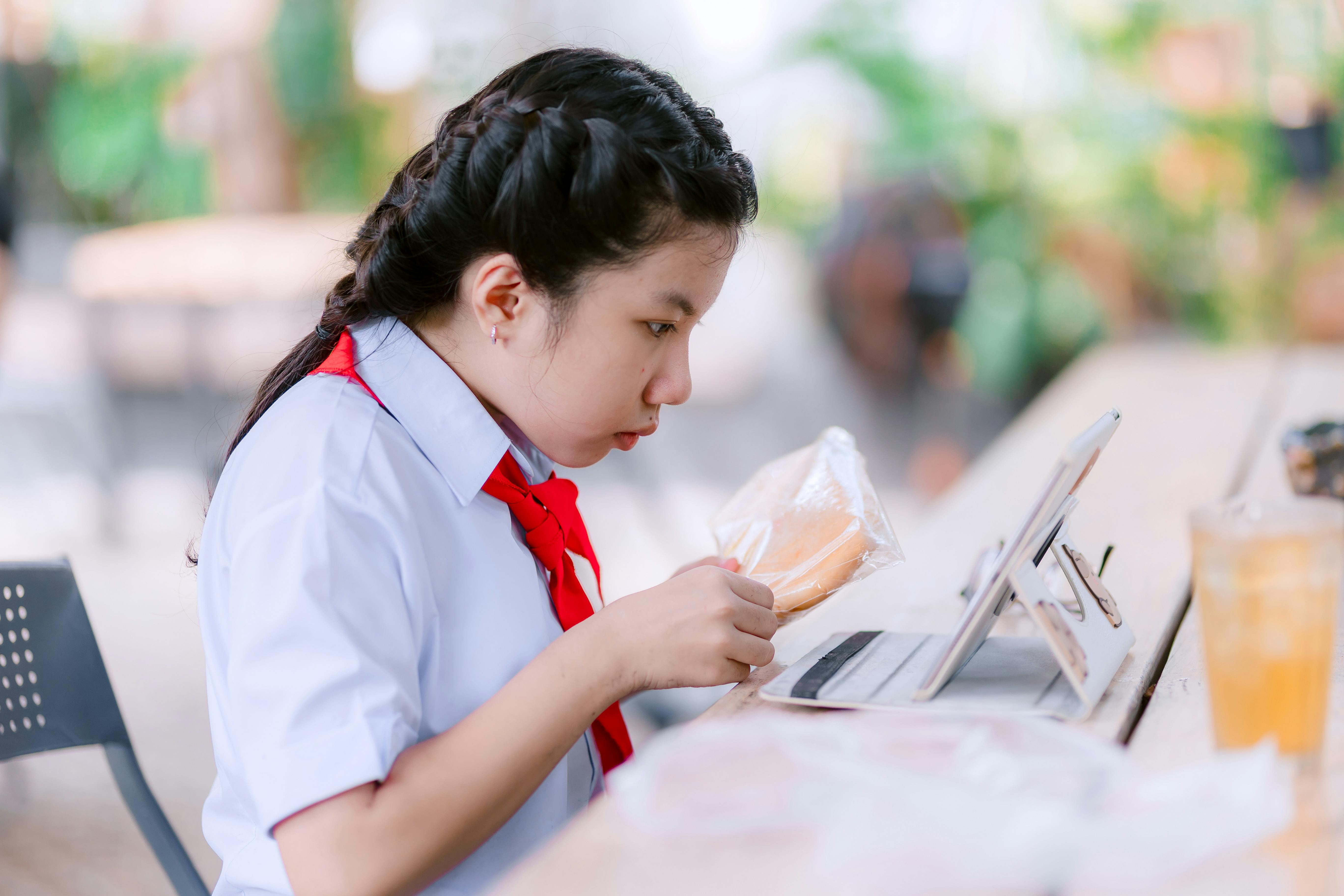 무료 교복을 입은 학생이 야외 카페에서 태블릿으로 공부하며 집중하고 있는 모습입니다. 스톡 사진