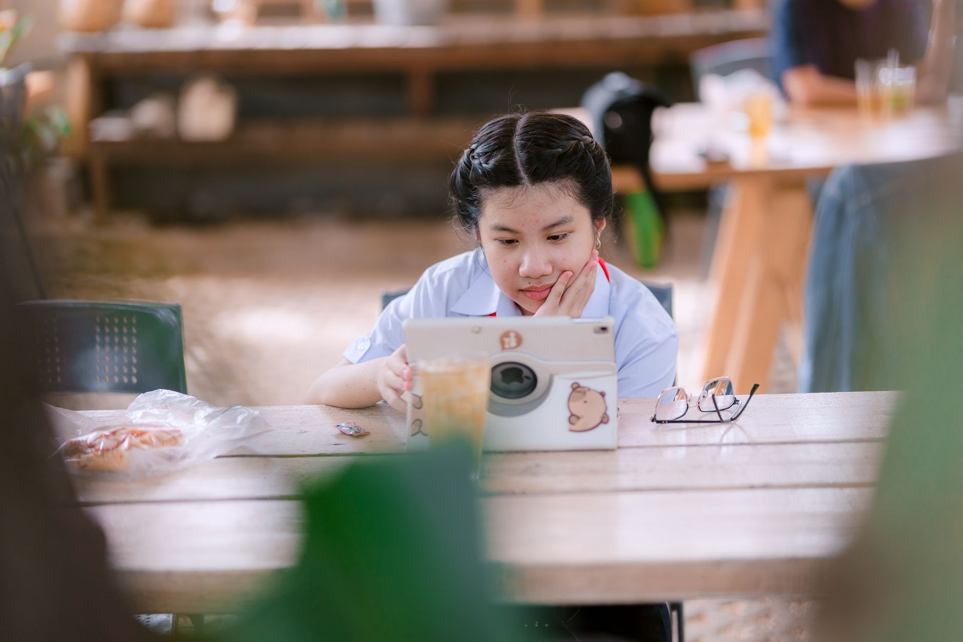 A young girl attentively using a tablet for learning while seated outdoors, enjoying a relaxed atmosphere.