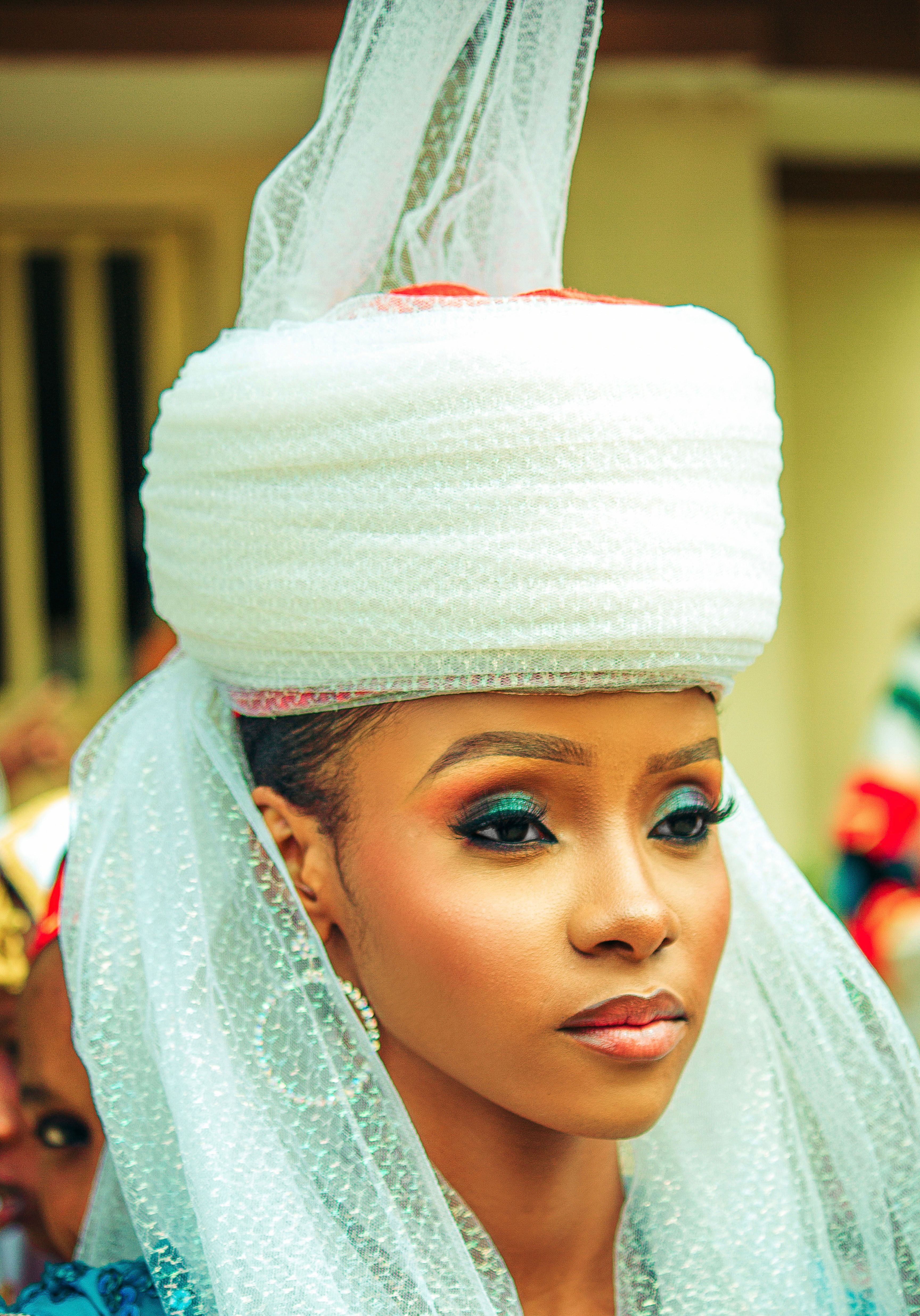 Portrait of a woman in traditional African attire with striking makeup and headpiece.