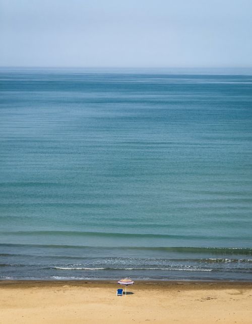 Free Serene beach scene with umbrella and chair by the calm sea, ideal for relaxation. Stock Photo