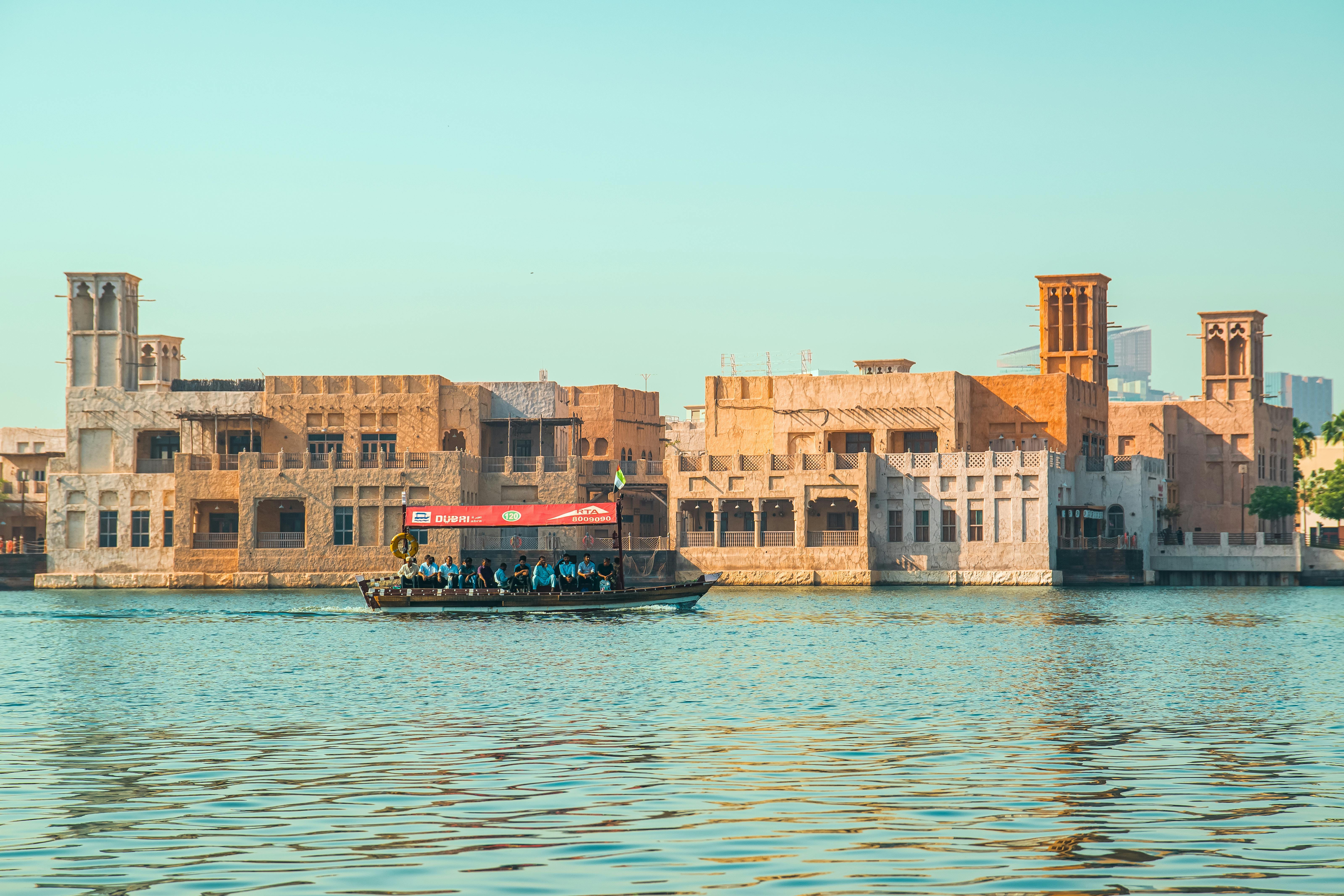 Abra boat sailing along Dubai Creek with traditional architecture in the background during sunset.