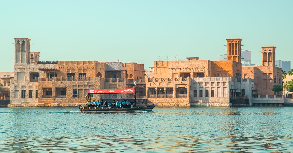 Abra boat sailing along Dubai Creek with traditional architecture in the background during sunset.
