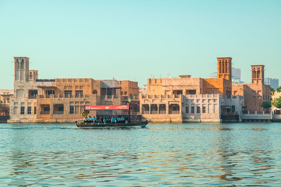 Traditional wooden Abra boat crossing Dubai Creek with historic buildings in the background
