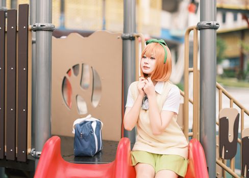 Young woman in a costume sitting on a playground slide with a thoughtful expression.